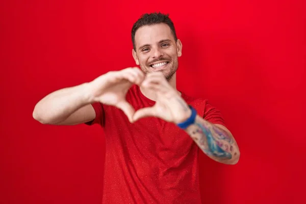 Jonge Spaanse Man Staat Rode Achtergrond Glimlachend Liefde Doen Hart — Stockfoto