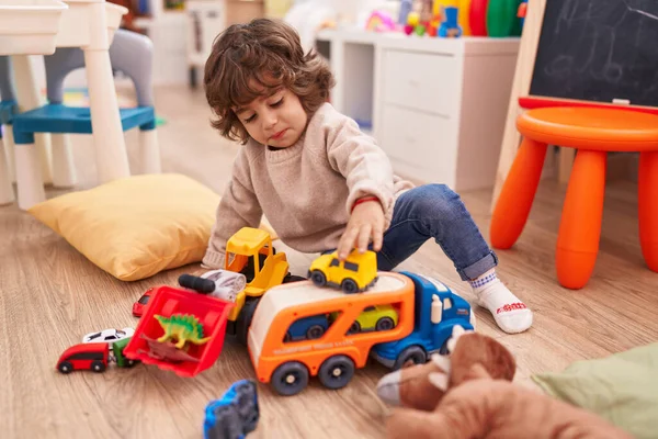 愛らしいヒスパニック男の子遊びます車おもちゃで床に座って幼稚園 — ストック写真