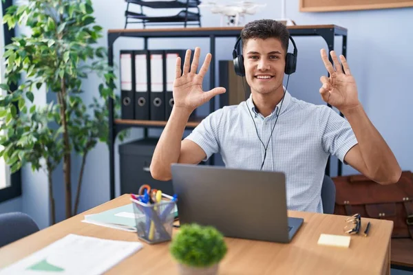自信と幸せな笑顔ながらヘッドフォンを着てオフィスで働いている若いヒスパニック系の男は 指の数8を示すと指摘します — ストック写真