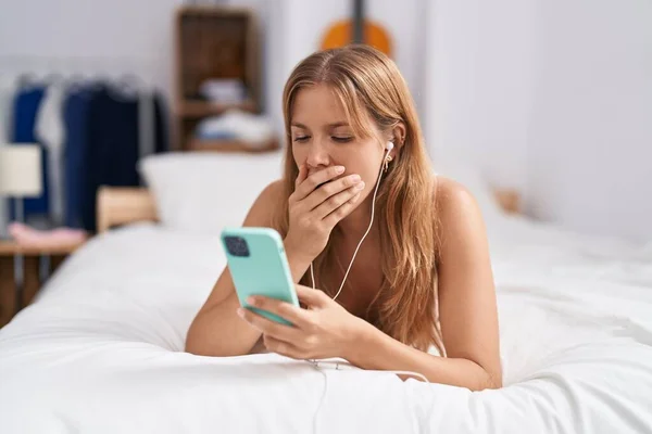 Young Blonde Girl Using Smartphone Earphones Tired Lying Bed Bedroom — 图库照片