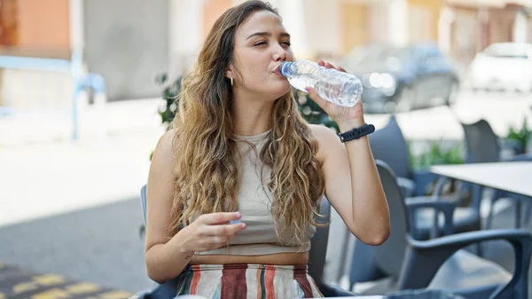 年轻美丽的惊慌失措的女人坐在咖啡店的阳台上喝着一瓶水 — 图库照片