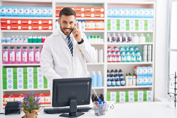 Young Hispanic Man Pharmacist Talking Telephone Using Computer Pharmacy — Stock Photo, Image