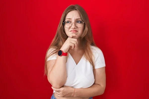 Молодая Белая Женщина Стоящая Красном Фоне Думая Вопросе Обеспокоенная Нервная — стоковое фото