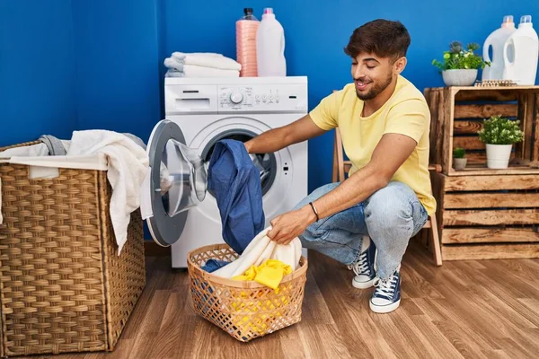 洗濯室で自信を持って洗濯服を笑っている若いアラブ人男性 — ストック写真