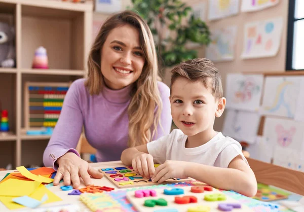 stock image Woman and boy playing with maths puzzle game sitting on table at kindergarten