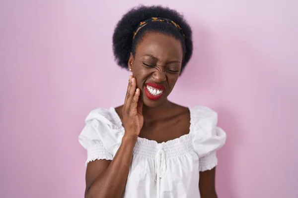 非洲妇女 卷曲的头发站在粉红的背景上 用手触摸着嘴 由于牙齿疼痛或牙齿疾病而有痛苦的表情 — 图库照片