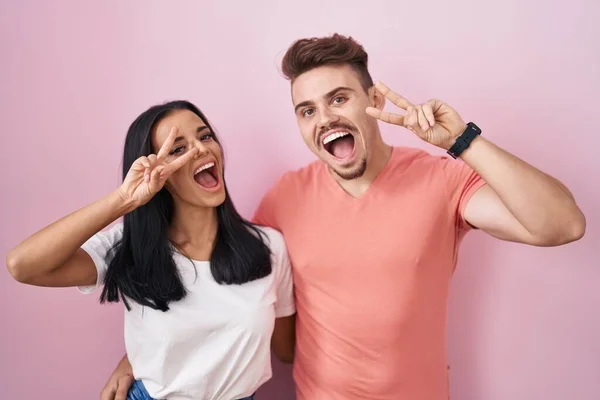 Young Hispanic Couple Standing Pink Background Doing Peace Symbol Fingers — Stockfoto