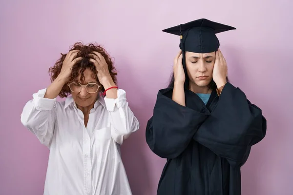 ヒスパニック系の母親と娘は 痛みや片頭痛のために必死の頭痛やストレスに苦しんで卒業キャップや儀式のローブを着て 手を頭に — ストック写真