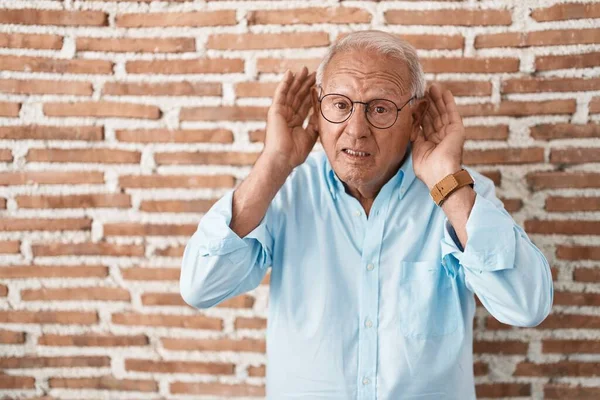 Homem Sênior Com Cabelos Grisalhos Sobre Parede Tijolos Tentando Ouvir — Fotografia de Stock