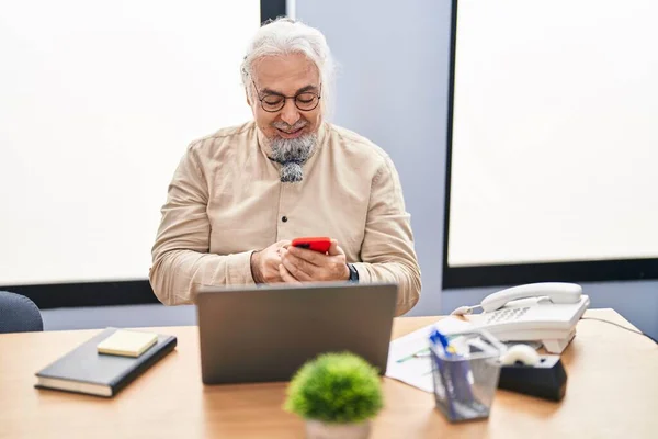 オフィスでノートパソコンやスマートフォンを使用している中世の白髪ビジネスワーカー — ストック写真
