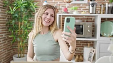 Genç sarışın kadın yemek odasındaki masada video görüşmesi yapıyor.