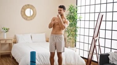 Genç İspanyol adam gülümseyerek yatak odasında dans ediyor.