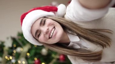 Genç ve güzel İspanyol kadın evdeki Noel ağacının yanında kanepeye oturmuş video görüşmesi yapıyor.