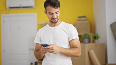 Genç İspanyol adam yeni evinde akıllı telefon kullanıyor.