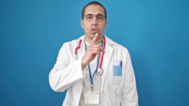 Genç İspanyol doktor, izole edilmiş mavi arka planda sessizlik istiyor.