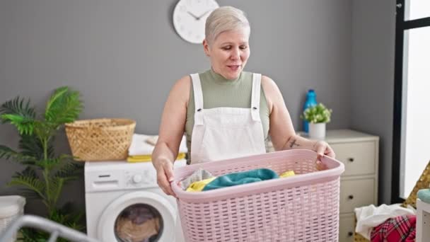 中年白髪の女性は洗濯室で服と自信を持って保持バスケット笑みを浮かべて — ストック動画