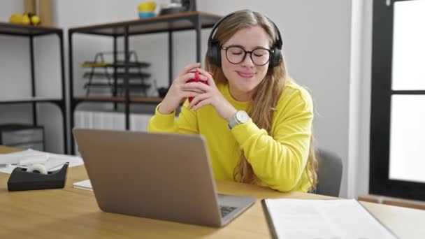 若いですブロンド女性ビジネス労働者に耳を傾け音楽を飲むコーヒーにオフィス — ストック動画