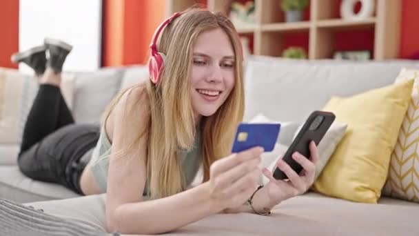 年轻的金发女人带着智能手机和信用卡购物 在家听音乐 — 图库视频影像
