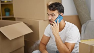 Genç İspanyol adam akıllı telefonda konuşuyor. Yeni evinde kazanan bir jestle koltukta oturuyor.