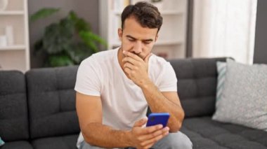 Evdeki kanepede oturan, akıllı telefon kullanan genç bir İspanyol.