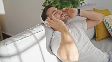 Genç İspanyol adam evdeki kanepede oturmuş müzik dinliyor.