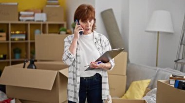 Orta yaşlı kadın yeni evinde akıllı telefondan konuşan kendinden emin bir şekilde gülümsüyor.