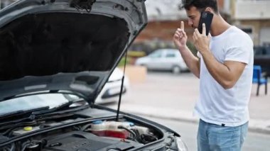 Genç İspanyol adam akıllı telefondan konuşuyor. Sokakta araba arızası sigortası var.
