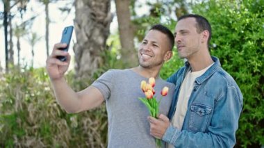 İki erkek parkta bir buket çiçekle akıllı telefondan selfie çekiyor.