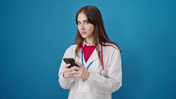 Νεαρή Ισπανίδα Γιατρός Χαμογελά Χρησιμοποιώντας Smartphone Απομονωμένο Μπλε Φόντο — Αρχείο Βίντεο