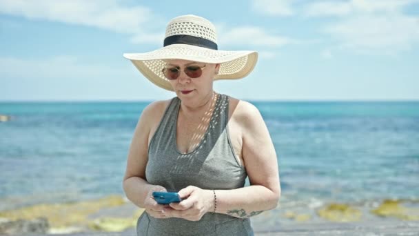 ビーチでスマートフォンを使って自信を持って笑顔中世の白髪の女性観光客 — ストック動画