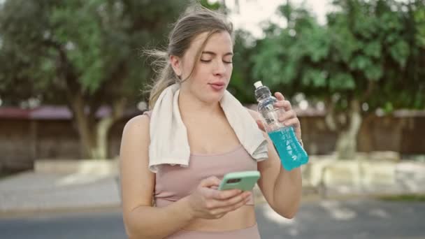 Jovem Loira Vestindo Roupas Esportivas Bebendo Bebida Energética Usando Smartphone — Vídeo de Stock