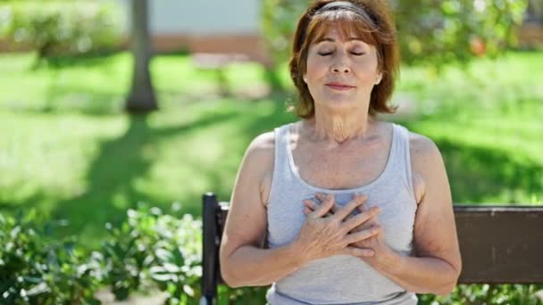 中年妇女双手放在胸前呼吸 坐在公园的长椅上 — 图库视频影像