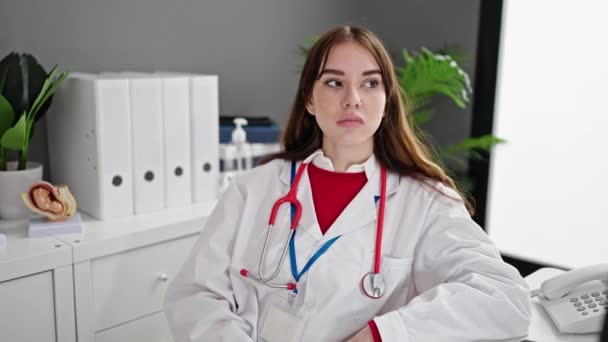 年轻的惊慌失措的女医生坐在桌子上微笑着在诊所里 — 图库视频影像
