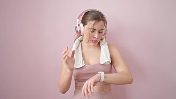 Mujer Rubia Joven Escuchando Música Mirando Cronómetro Sobre Fondo Rosa — Vídeo de stock