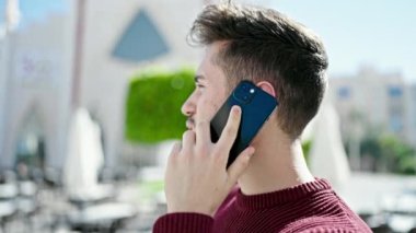 Genç İspanyol adam gülümsüyor. Kafe terasında akıllı telefondan konuşuyor.