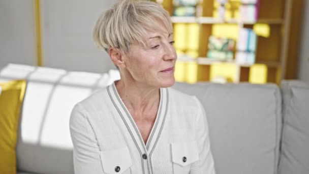 Blonde Frau Mittleren Alters Lächelt Selbstbewusst Auf Dem Sofa Sitzend — Stockvideo