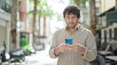 Genç İspanyol adam gülümsüyor. Akıllı telefon kullanıyor. Kazanan sokak jesti.