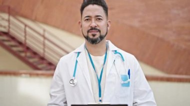 Genç Latin doktor gülümsüyor. Hastanede tıbbi raporu tutuyor.