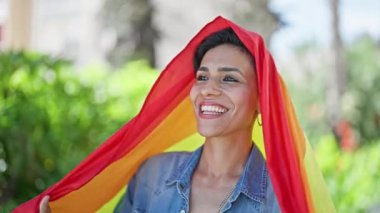 Parkta gökkuşağı bayrağı tutan güzel İspanyol kadın gülümsüyor.