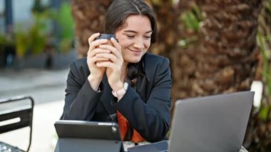 Laptop ve dokunmatik ped kullanan, kahve dükkanının terasında kahve içen genç ve güzel İspanyol iş kadını.