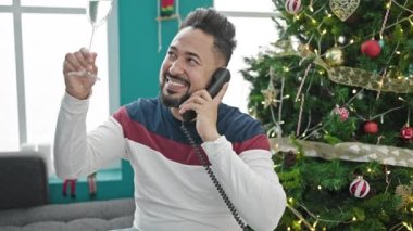 Genç Latin adam telefonda konuşuyor. Yılbaşı için kadeh kaldırıyor.