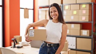 Young beautiful hispanic woman ecommerce business worker holding package at office