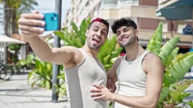 Gülümseyen iki erkek parkta akıllı telefondan özçekim yapıyor.
