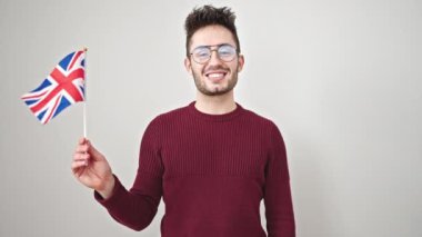 Genç İspanyol adam gülümsüyor. Birleşik krallık bayrağını soyutlanmış beyaz arka planda tutuyor.
