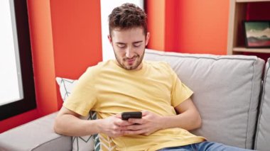 Evdeki kanepede oturan, akıllı telefon kullanan genç bir İspanyol.