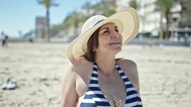 中年惊慌失措的女人坐在沙滩上的毛巾上晒日光浴 — 图库视频影像