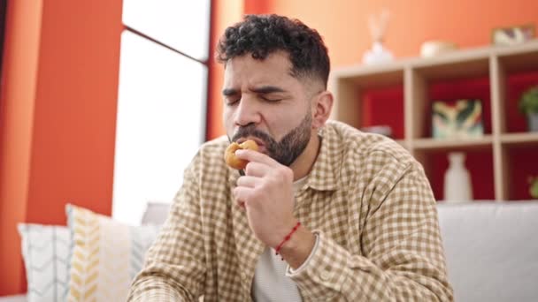 Joven Hispano Comiendo Donut Sentado Sofá — Vídeo de stock