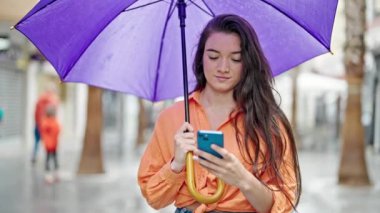 Sokakta akıllı telefon kullanan güzel İspanyol bir kadın şemsiye tutuyor.