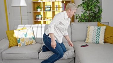 Orta yaşlı, kır saçlı, dans eden, akıllı telefondan müzik dinleyen bir kadın.