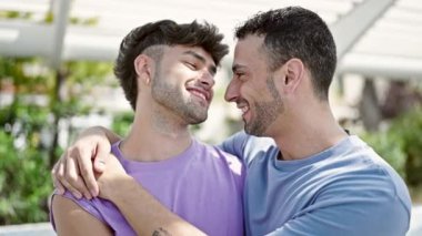 Two men couple smiling confident hugging each other at park
